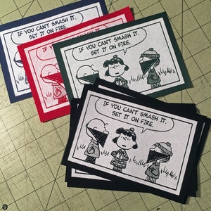 May include: Four black and white iron-on patches with the text "If you can't smash it, set it on fire." and a cartoon image of three characters wearing masks. The characters are wearing hats and have different facial expressions.