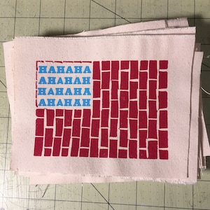 May include: A stack of white fabric patches with a red brick pattern and the text "HAHAHA AHAHAH HAHAHA AHAHAH" printed in blue.