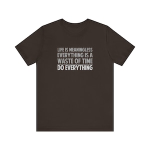 May include: A dark brown t-shirt with the text "LIFE IS MEANINGLESS EVERYTHING IS A WASTE OF TIME DO EVERYTHING" printed in grey.