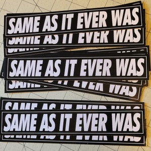 May include: A stack of black and white stickers with the text "SAME AS IT EVER WAS" repeated on each sticker.