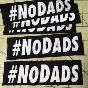 Puede incluir: Cuatro parches de tela negra con texto blanco que dice "#NODADS".