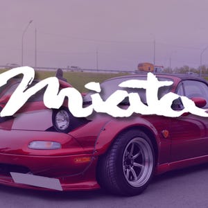 May include: A red Miata sports car with pop-up headlights and custom wheels. The word "Miata" is written in white script across the car's hood. The car is parked outdoors, with a blurred background.
