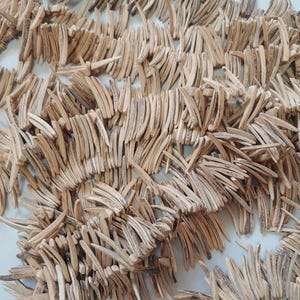 May include: A close-up of a pile of natural wood pieces, each with a curved shape and a light brown color. The pieces are arranged in a random pattern, creating a textured and organic look.