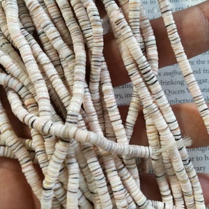 May include: A strand of white, brown, and pink shell beads. The beads are small and round, and they are strung together on a thin thread.