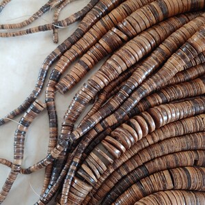 May include: A strand of brown and black coconut shell beads. The beads are round and flat, and they are strung together on a thin cord.