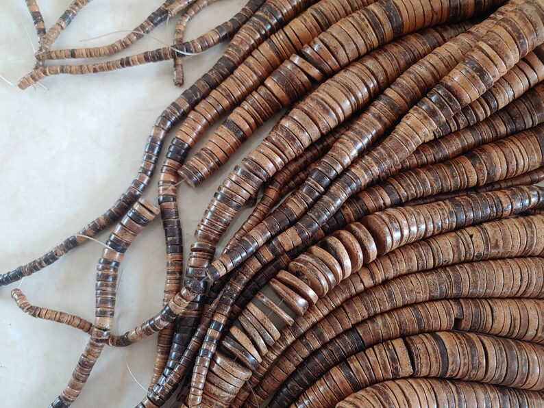 May include: A strand of brown and black coconut shell beads. The beads are round and flat, and they are strung together on a thin cord.