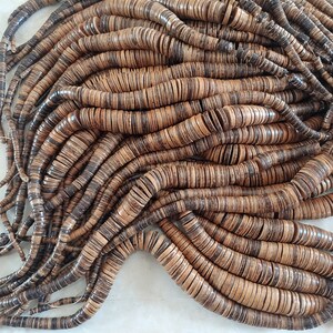 May include: A large pile of brown and tan coconut shell beads. The beads are round and flat, and they are strung together on a string. The beads are arranged in a random pattern, and they are all the same size.