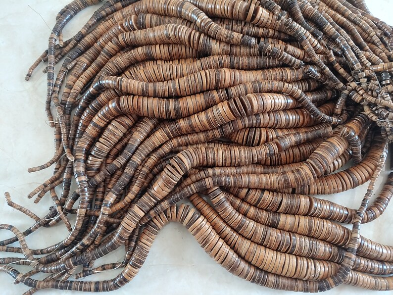 May include: A large pile of brown and tan coconut shell beads. The beads are round and flat, and they are strung together on a string. The beads are arranged in a random pattern, and they are all the same size.