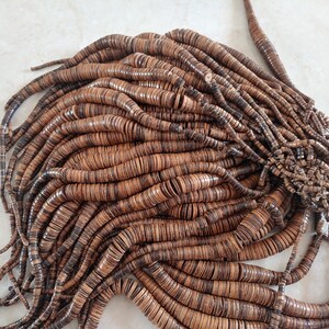 May include: A large pile of brown wooden beads, each bead is a flat disc with a hole in the centre. The beads are arranged in a random pattern, creating a textured and organic look.
