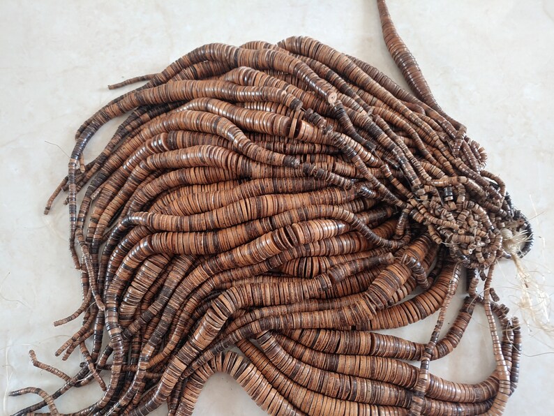 May include: A large pile of brown wooden beads, each bead is a flat disc with a hole in the centre. The beads are arranged in a random pattern, creating a textured and organic look.