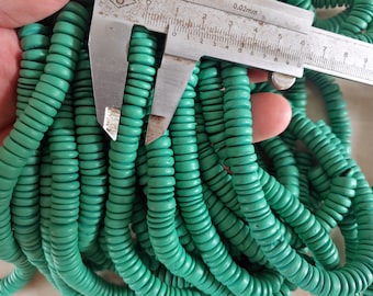 May include: A close-up of a pile of turquoise green wooden beads. The beads are round and have a slightly textured surface. A ruler is used to measure the size of the beads, which are approximately 0.6 cm in diameter.