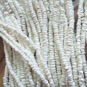 May include: A close-up of a strand of white shell beads. The beads are small and round, and they are strung together on a thin thread. The beads are all the same size and shape, and they are arranged in a uniform pattern.