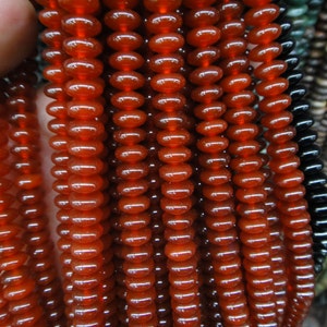 May include: A strand of red carnelian beads, each bead is oval shaped and polished smooth. The beads are strung together on a clear thread.