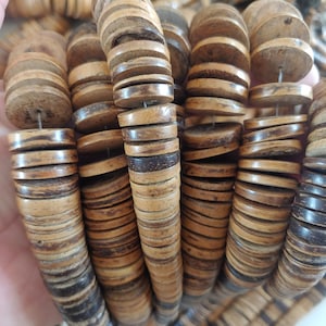 Peut inclure: Gros plan sur un collier composé de perles rondes en bois naturel. Les perles sont brun clair avec des accents brun foncé, enfilées sur un fil fin. Le collier a une esthétique rustique et terreuse, adaptée à un style bohème ou décontracté.