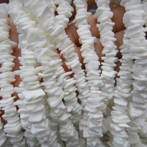 Peut inclure: Un brin de perles de coquillage blanches, chaque perle est de forme plate et irrégulière, avec une texture légèrement rugueuse.