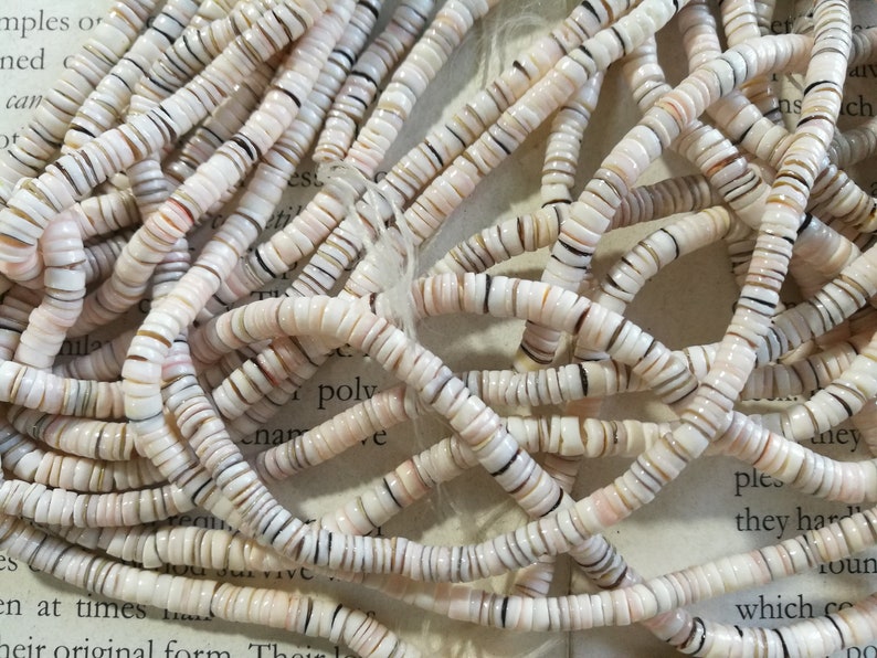 May include: A close-up of a pile of white, brown, and black shell beads. The beads are small and round, and they are arranged in a random pattern.