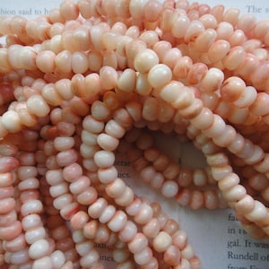 Könnte beinhalten: Eine Schnur aus rosa und weißen Muschelperlen. Die Perlen sind klein und rund und haben eine leicht unregelmäßige Form. Die Perlen sind auf einer durchsichtigen Schnur aufgefädelt.