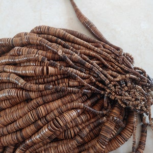 May include: A large pile of brown wooden beads, each bead is a flat disc with a hole in the centre. The beads are arranged in a random pattern, creating a textured and organic look.