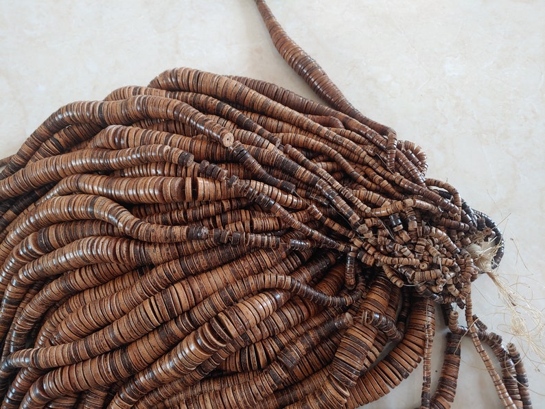 May include: A large pile of brown wooden beads, each bead is a flat disc with a hole in the centre. The beads are arranged in a random pattern, creating a textured and organic look.