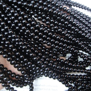 Può includere: Una collana di perle di onice nero. Le perle sono rotonde e lisce e sono infilate su un filo trasparente.