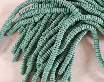 May include: A strand of teal green wooden beads. The beads are round and have a slightly irregular shape. The beads are strung on a clear thread.