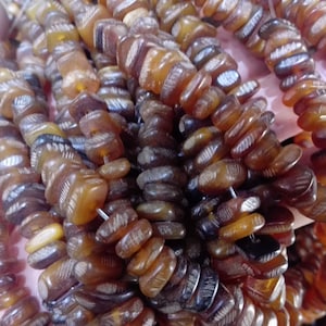 以下が含まれることがあります： 彫刻されたデザインの茶色と琥珀色のビーズのストランド。ビーズは細いワイヤーに糸で通されており、直径は約1.2cmです。