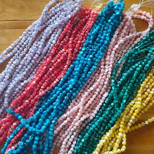 May include: Multiple strands of small, round, faceted beads in various colours including lavender, red, bright blue, light pink, dark green, and yellow. Each bead features a subtle, marbled or speckled pattern throughout the surface.