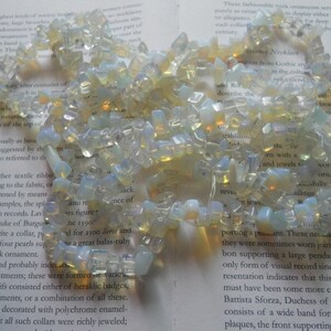 May include: A strand of iridescent opal gemstone beads, strung together to form a necklace. The beads are various shapes and sizes, with a milky white and pale yellow color.