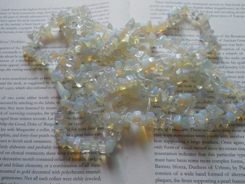 May include: A strand of iridescent opal gemstone beads, strung together to form a necklace. The beads are various shapes and sizes, with a milky white and pale yellow color.