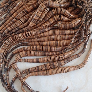 May include: A strand of brown and black coconut shell beads. The beads are round and flat, and they are strung together on a thin cord.
