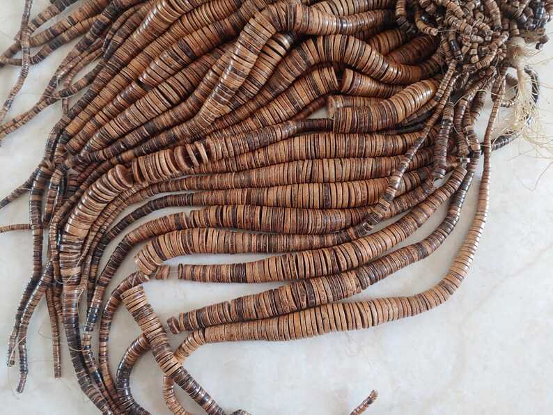 May include: A strand of brown and black coconut shell beads. The beads are round and flat, and they are strung together on a thin cord.