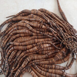 May include: A large pile of brown wooden beads, each bead is a flat disc with a dark brown centre and a lighter brown outer edge.