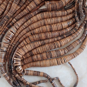 May include: A strand of brown and tan coconut shell beads. The beads are round and flat, and they are strung together on a thin cord.
