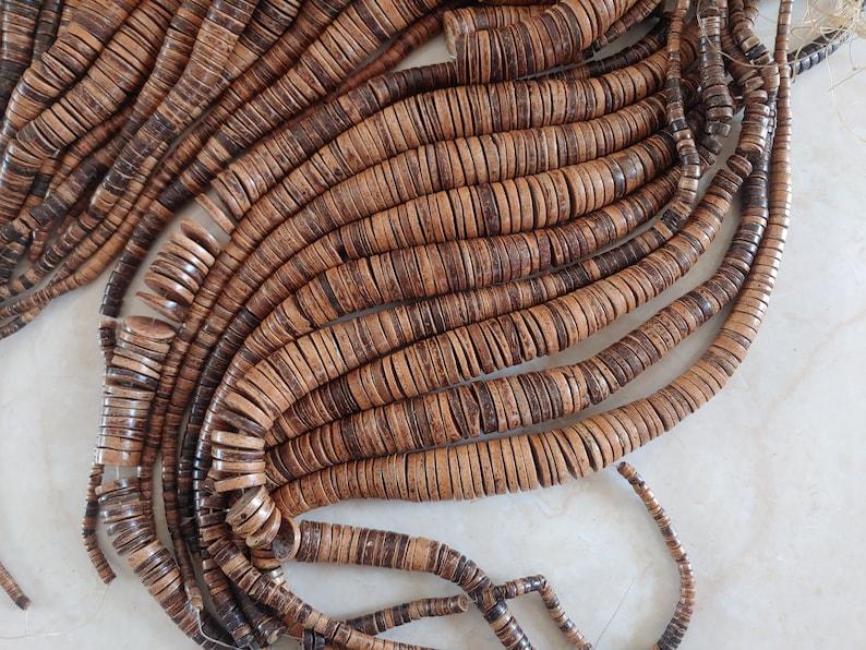 May include: A strand of brown and tan coconut shell beads. The beads are round and flat, and they are strung together on a thin cord.