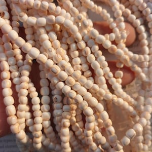Peut inclure: Gros plan sur plusieurs brins de perles ovales blanc cassé. Les perles ont un aspect naturel et organique avec de subtiles variations de couleur et de texture. Les perles sont enfilées ensemble, créant une surface fluide et texturée.