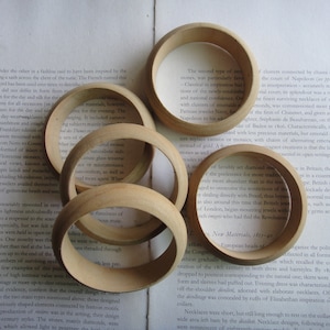 Puede incluir: Primer plano de varios brazaletes de madera, algunos con tallas intrincadas, dispuestos en una página de un libro con texto sobre joyería y materiales. El texto menciona el uso de camafeos, esmeraldas y diamantes en joyería.