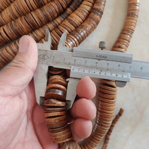 May include: Close-up of a wooden bead necklace with a ruler measuring the diameter of the beads at 1.6 cm. The beads are a light brown colour with darker brown streaks.
