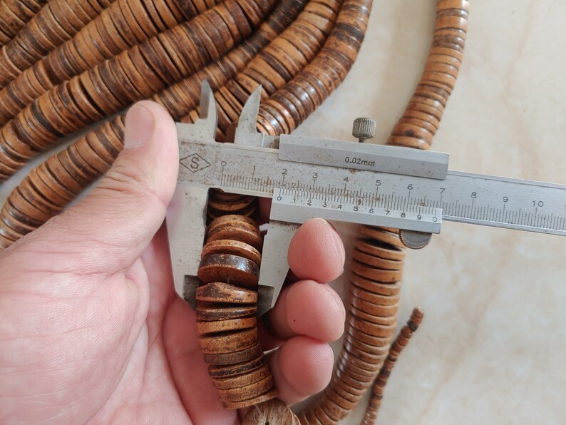 May include: Close-up of a wooden bead necklace with a ruler measuring the diameter of the beads at 1.6 cm. The beads are a light brown colour with darker brown streaks.