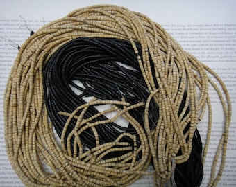May include: A close-up of a pile of black and cream-colored beads. The beads are made of wood and are strung together in long strands.
