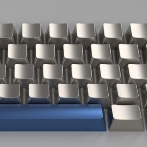 Puede incluir: Un teclado plateado con una barra espaciadora azul. Las teclas son todas rectangulares y tienen un borde ligeramente redondeado.
