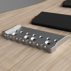 May include: Close-up of a light wood guitar body with a silver bridge and black pickup covers.