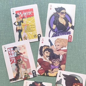 May include: A collection of playing cards featuring stylized illustrations of female characters. The cards display various suits and numbers, with some cards showcasing text like "MAGIC" and "Catwoman". The color palette includes red, black, and purple.