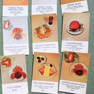 May include: A collection of vintage menu cards featuring various dishes. The cards showcase items like vegetable soup, ham cold plate, tossed salad, chopped sirloin steak, summer suggestion, Masterburger, filet mignon, and two eggs scrambled.