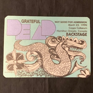 May include: A vintage backstage pass with the words "Grateful Dead" in purple and a detailed illustration of a mythical creature. The pass is teal and includes the date March 22, 1990, and the location, Copps Coliseum, Hamilton Ontario, Canada.