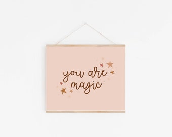May include: A pink poster with the text "you are magic" in brown cursive script. The poster is decorated with small gold and red stars.