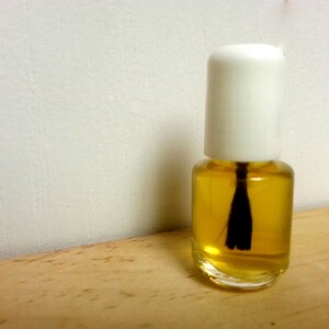 May include: A small clear glass bottle with a white cap and a black applicator brush filled with a yellow liquid.