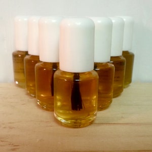 May include: A group of ten small, clear glass bottles with white caps filled with a light amber liquid. The bottles are arranged in a triangular shape on a light brown wooden surface.