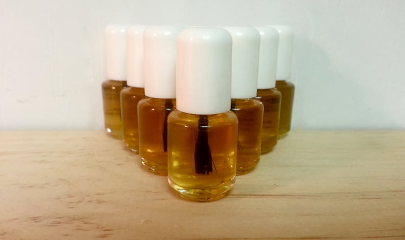 May include: A group of ten small, clear glass bottles with white caps filled with a light amber liquid. The bottles are arranged in a triangular shape on a light brown wooden surface.