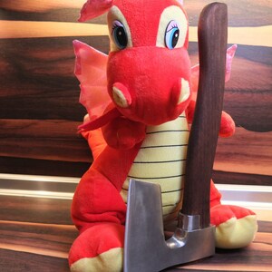May include: A red plush dragon toy holding a small, silver-colored axe with a brown wooden handle.