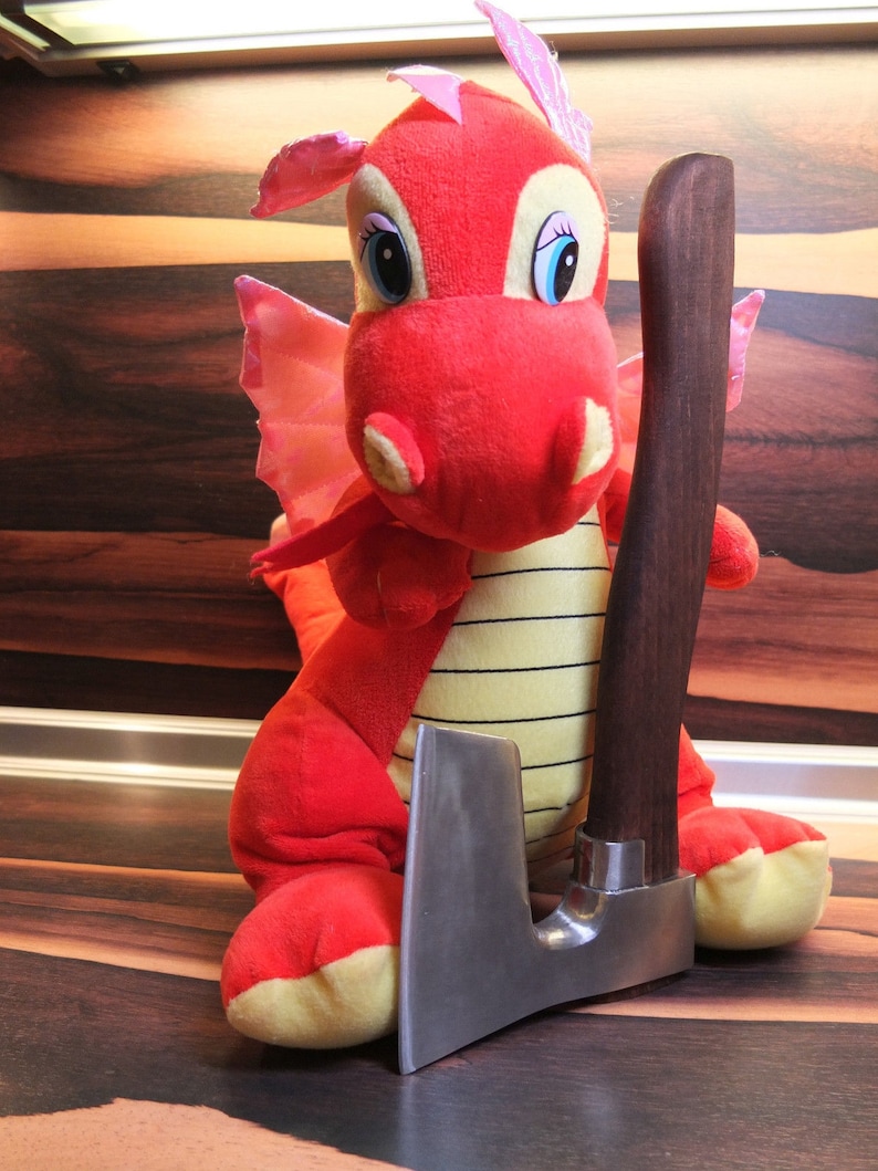 May include: A red plush dragon toy holding a small, silver-colored axe with a brown wooden handle.